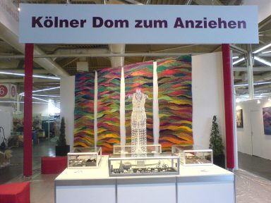 Kunstinstallation mit einem weißen Gewand und farbenfrohem Hintergrund im Kölner Dom.