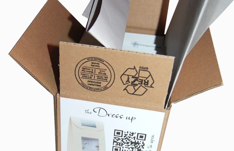 Offene Kartonage mit QR-Code und Recycling-Symbol, Inhalt sichtbar.