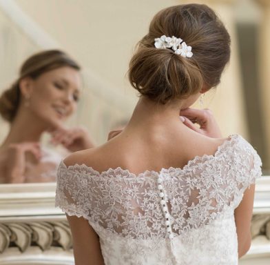 Braut in einem Spitzenkleid mit schickem Haarschmuck, blickt in den Spiegel.