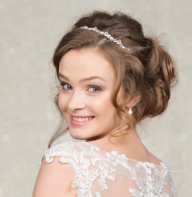 Braut mit lockigem Haar und Perlenhaarschmuck, lächelnd in eleganter Hochzeitskleidung.